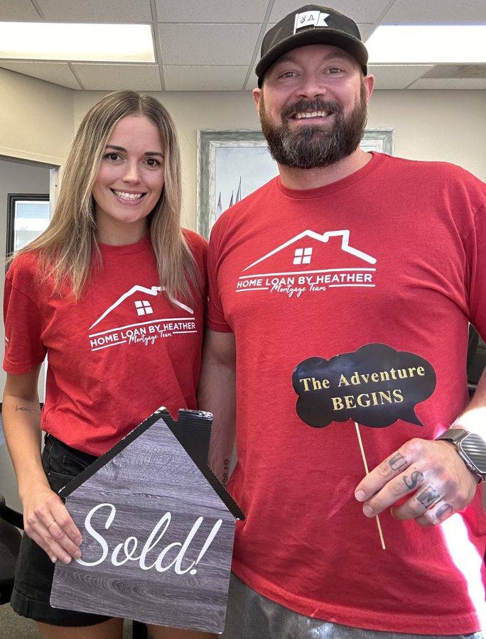Two people with a Sold! sign after a closing